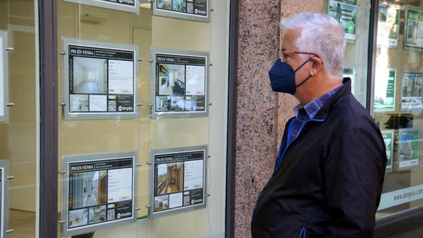 Pla mitjà d'una persona mirant les ofertes de pisos a un aparador d'una immobiliària.